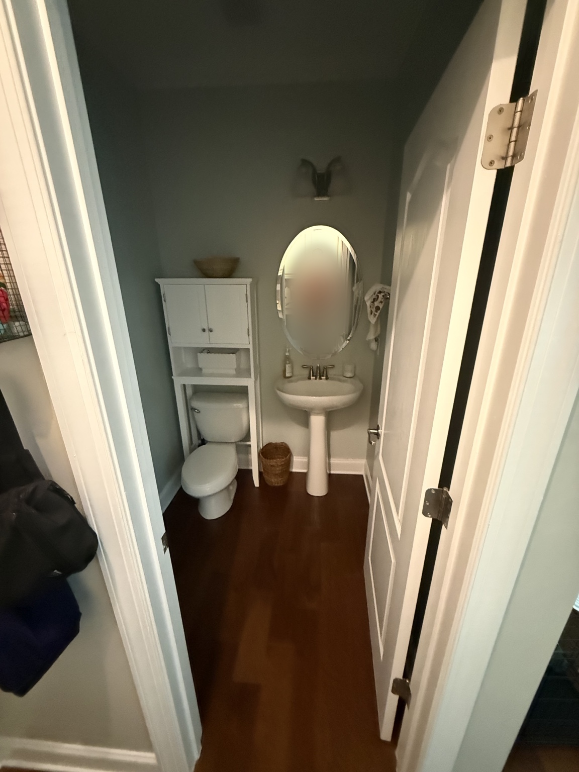 Powder room before with wood flooring and the photographer's reflection blurred in the mirror
